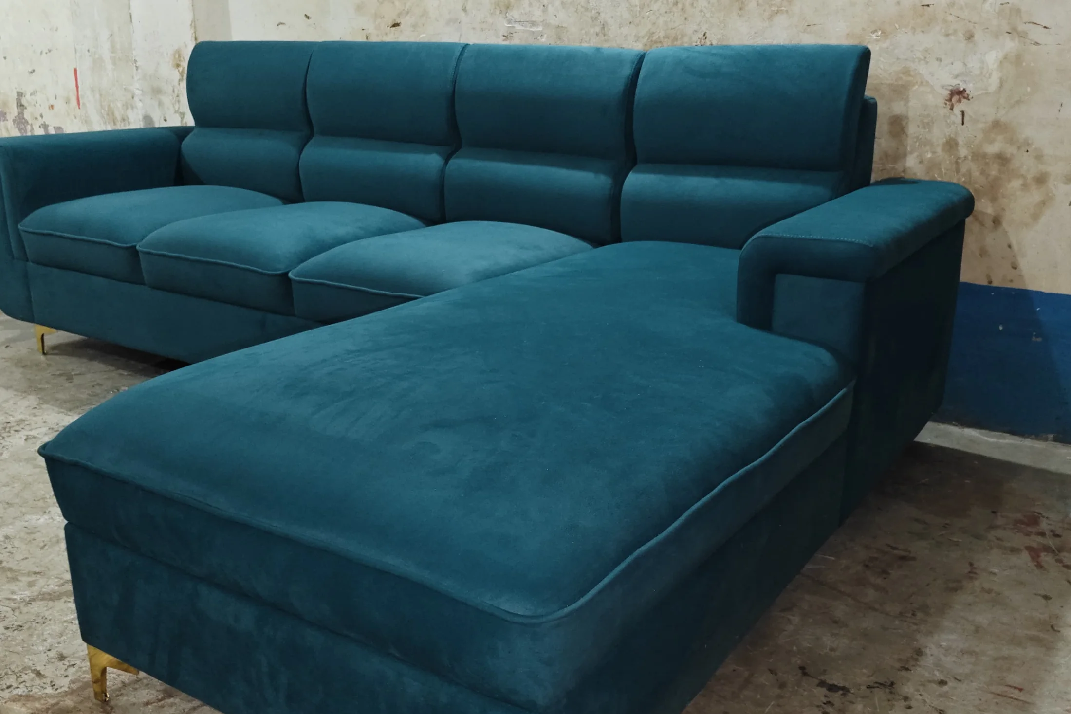 A teal velvet L-shape sofa with brass legs, newly finished and standing on the workshop floor in Topsia.